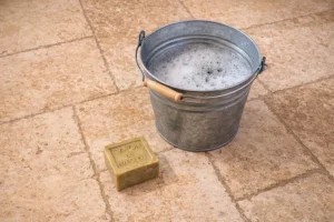 Seau mousseux et savon de Marseille sur carrelage.